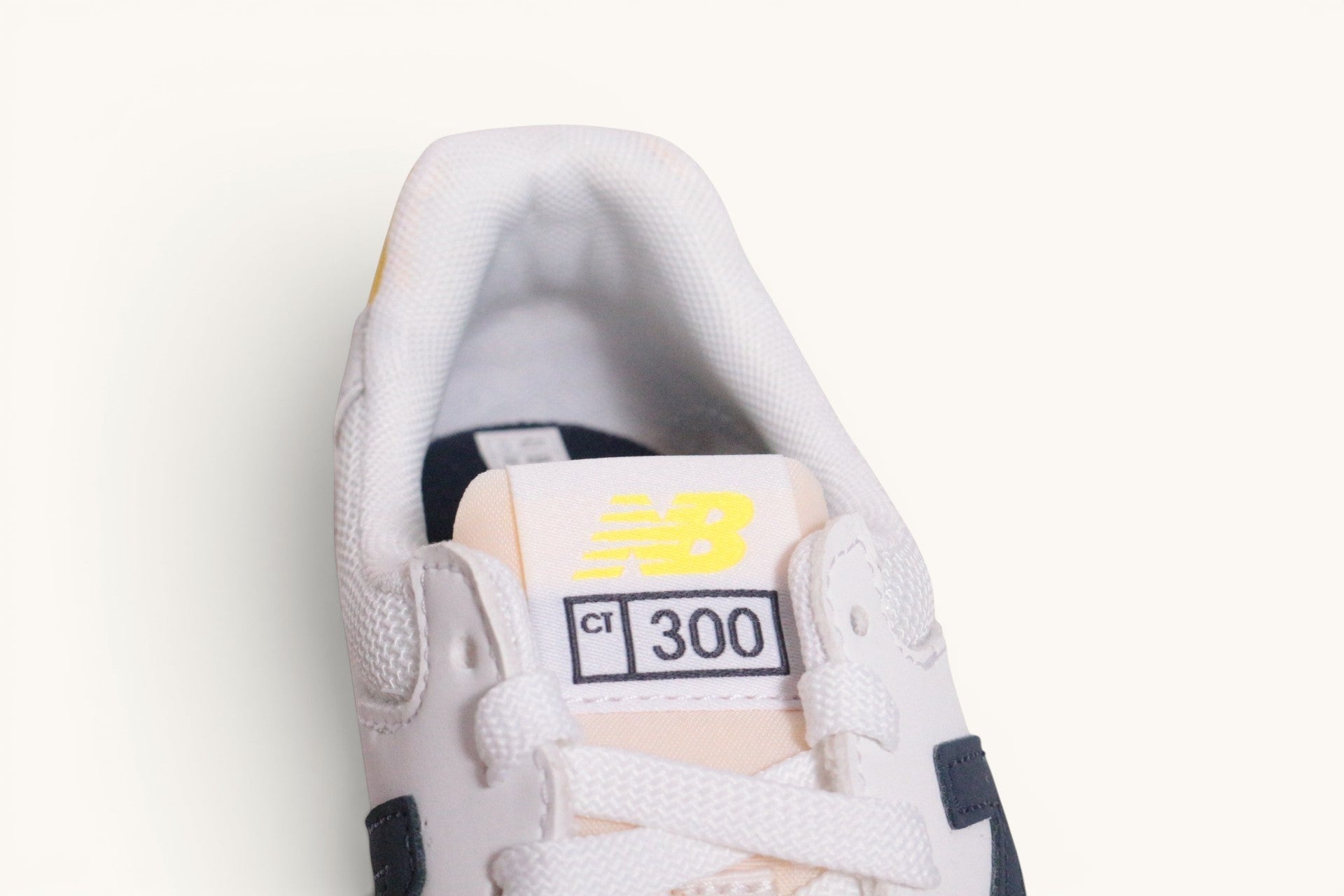 Baskets New Balance CT300 blanches en cuir avec détails bleu marine et logo jaune, proposées par Frippindealz.