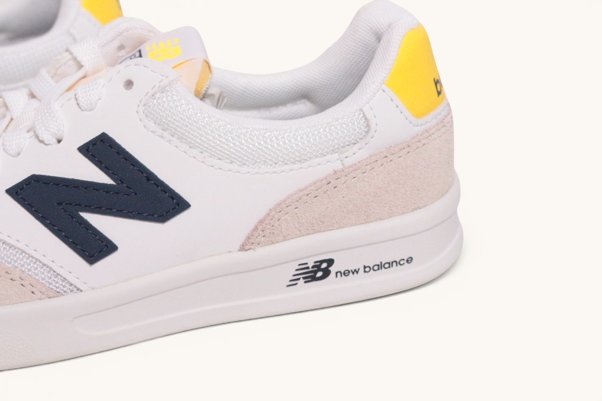 Baskets New Balance Frippindealz en cuir blanc avec logo bleu marine et détails jaunes, vue latérale