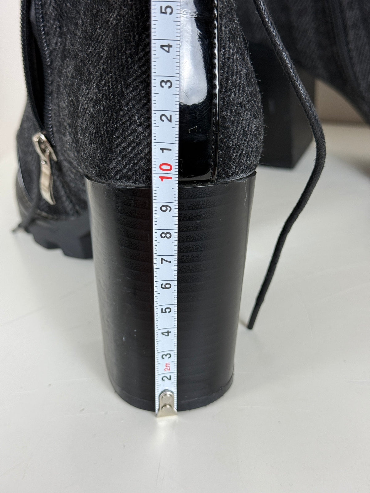 Gros plan sur le talon épais de 10 cm d'une bottine Frippindealz noire en cuir verni et laine avec mètre ruban