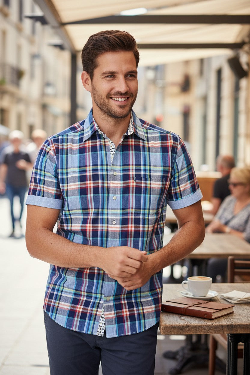 Homme souriant portant une chemise Marvelis à carreaux bleus et multicolores en coton avec manches courtes à revers.