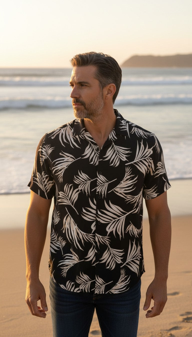Homme portant une chemise Frippindealz H&M noire en viscose à motif feuillage et col bowling sur une plage au coucher