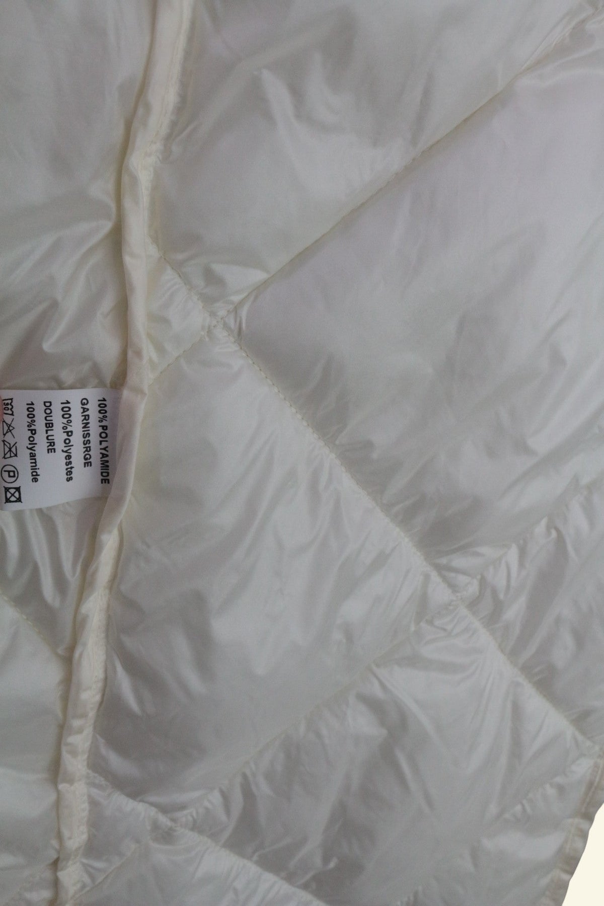 Détail de la doublure matelassée crème de la doudoune longue Freda chez Frippindealz avec étiquette de composition