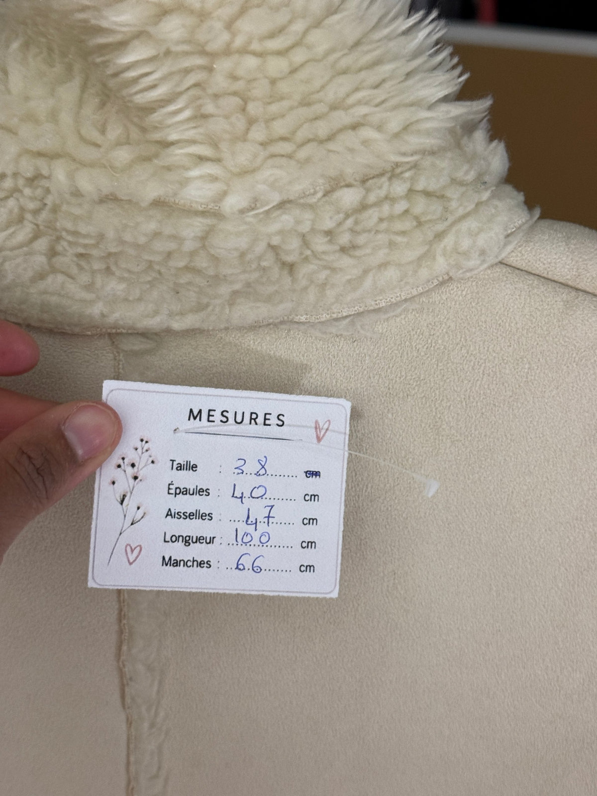 Étiquette de mesures Frippindealz sur un manteau en fausse fourrure blanc avec détails en polyester