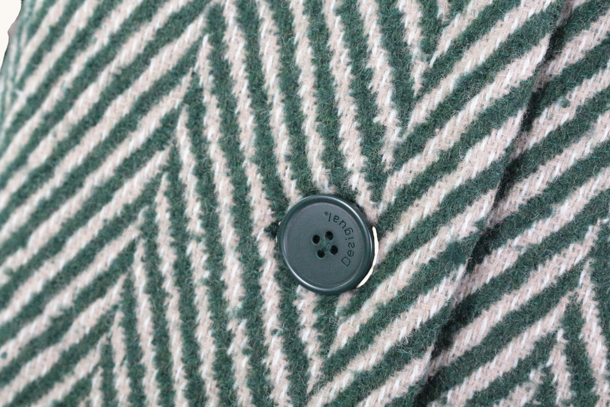 Gros plan sur le motif chevron vert et beige du manteau en laine Frippindealz avec un bouton siglé Desigual