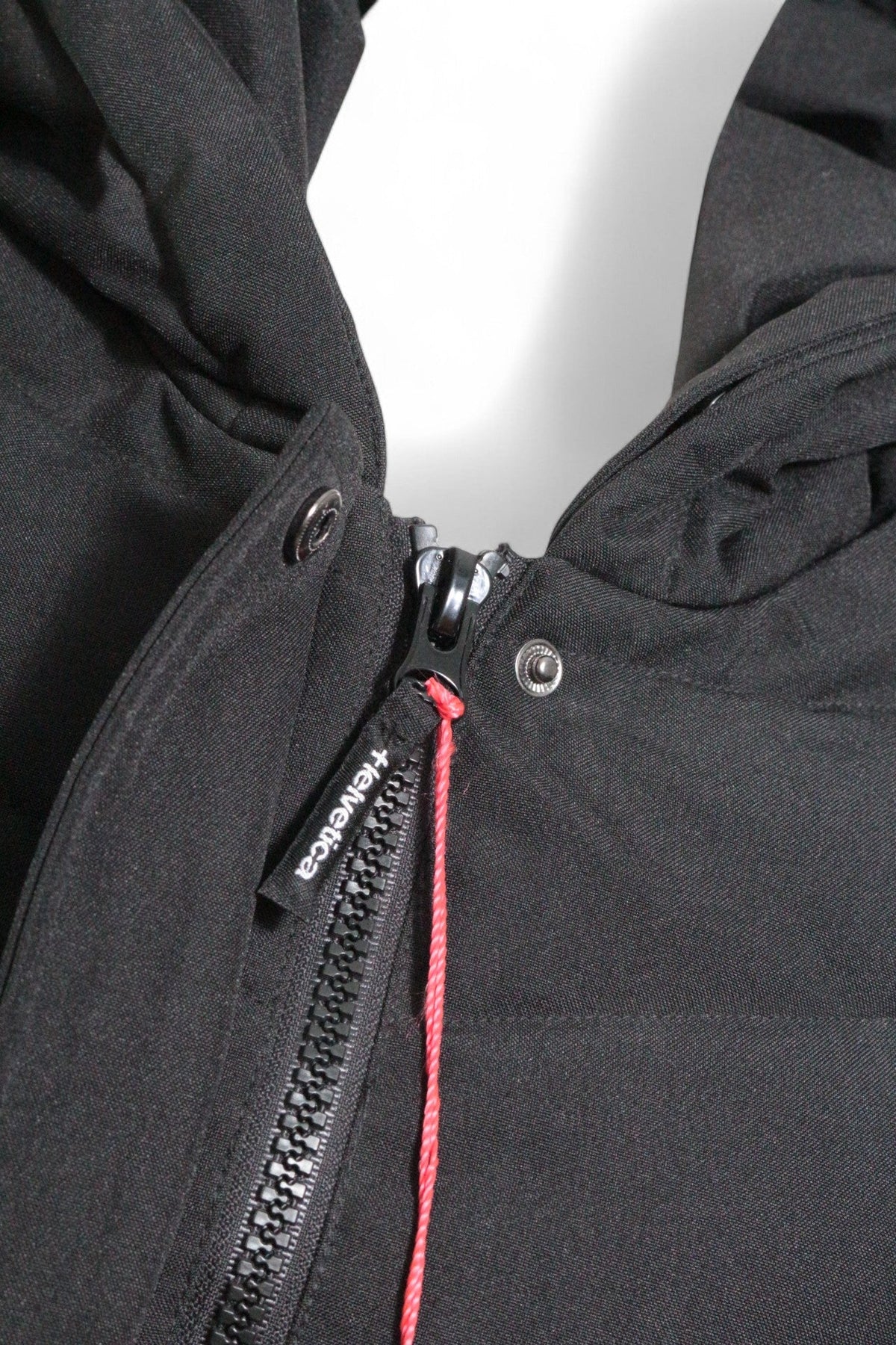 Détail de la fermeture éclair noire avec tirette marquée Helvetica sur une parka Frippindealz en polyester noir