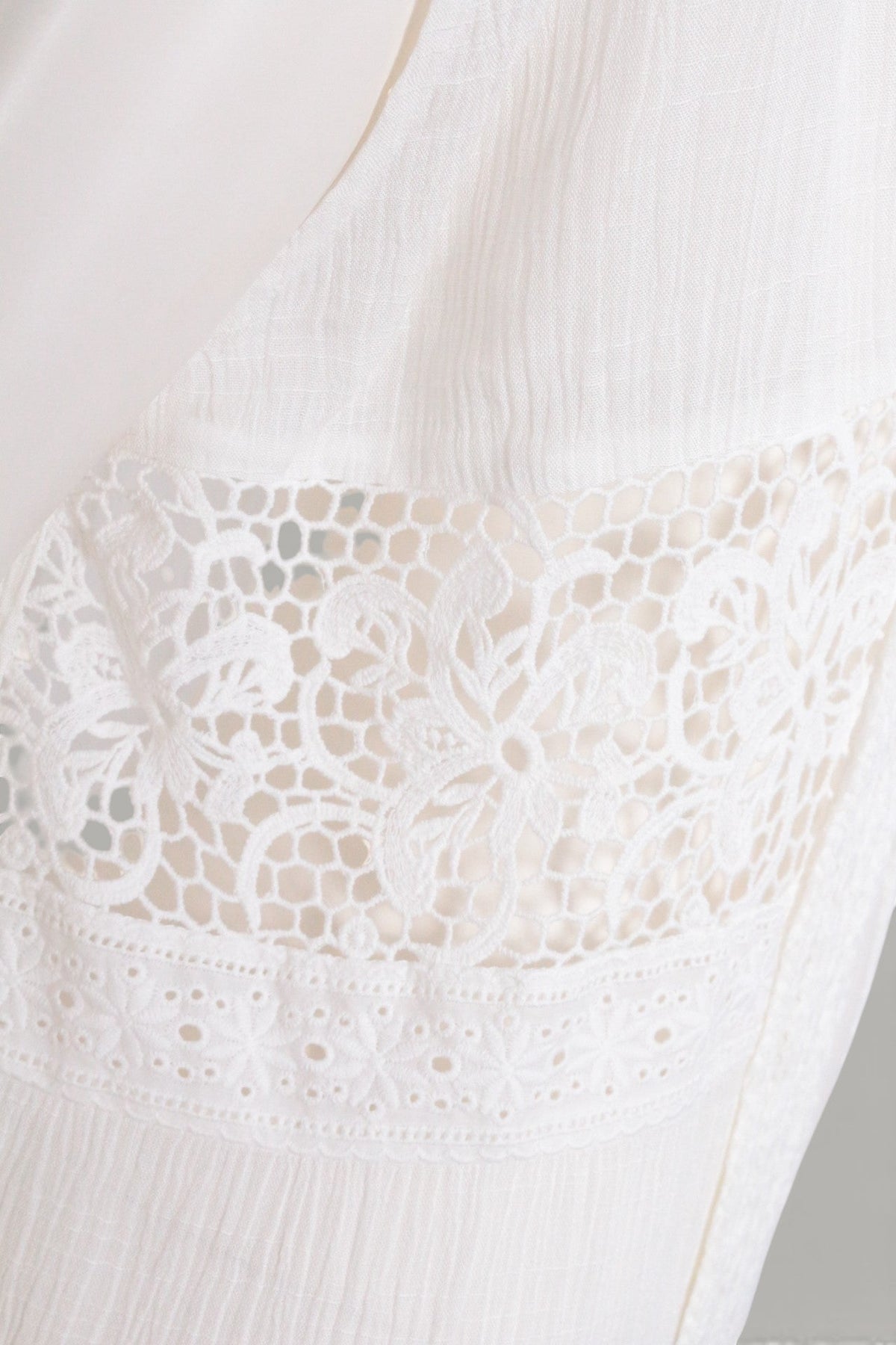 Détail en gros plan du poncho Frippindealz en dentelle crème avec des motifs floraux délicats et ajourés