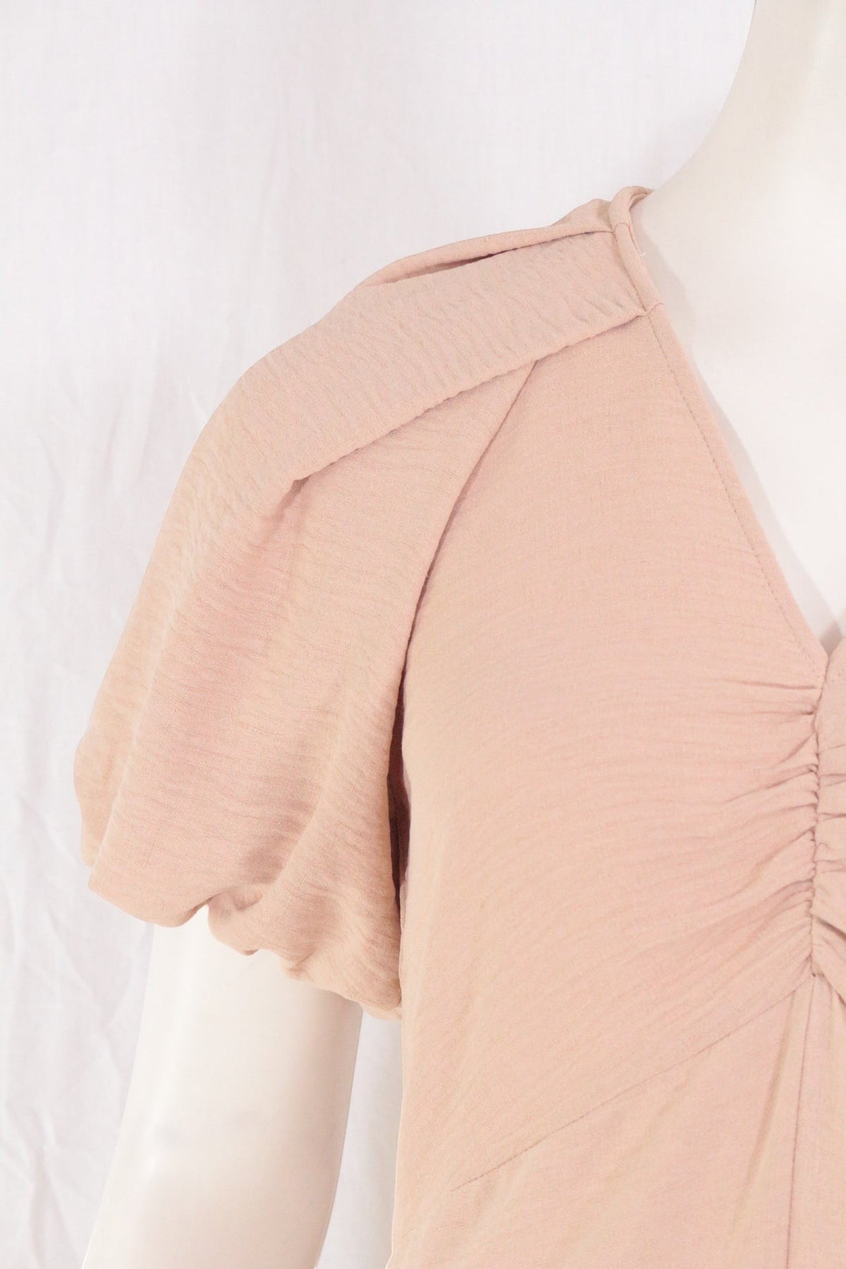Gros plan sur la manche bouffante et le décolleté drapé de la robe longue beige Frippindealz en polyester