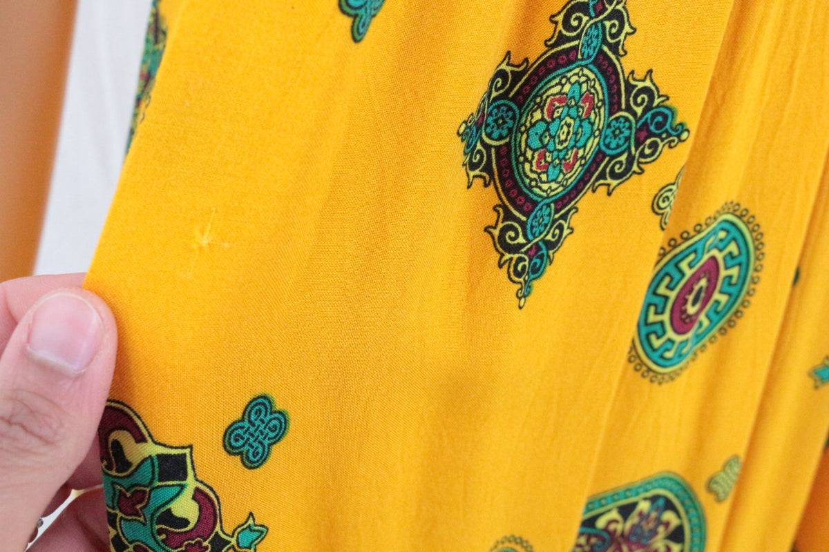 Gros plan sur le tissu en coton jaune d'une robe longue Frippindealz avec des motifs berbères colorés.