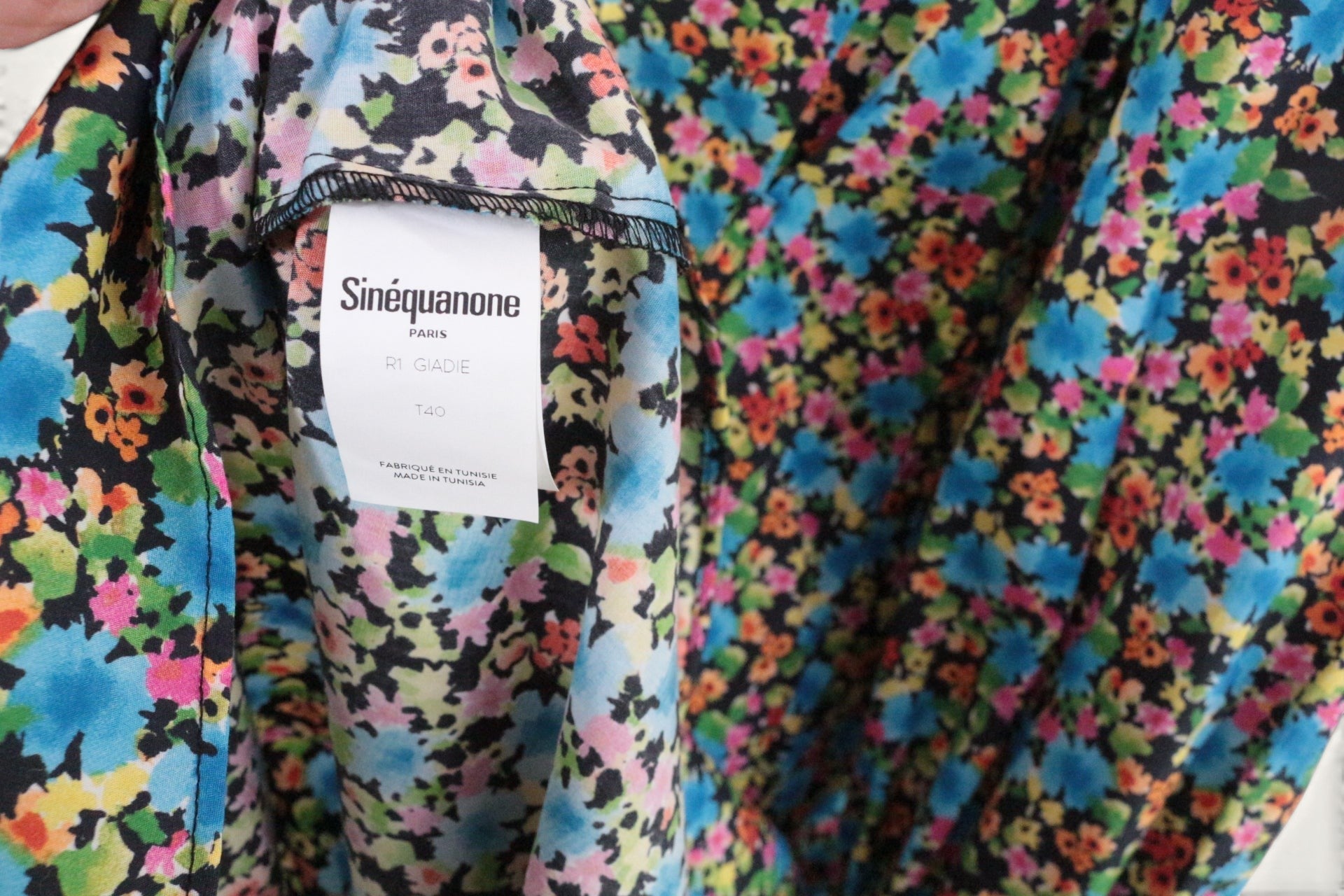 Gros plan sur l'étiquette Frippindealz et le tissu en polyester à imprimé floral multicolore sur fond noir