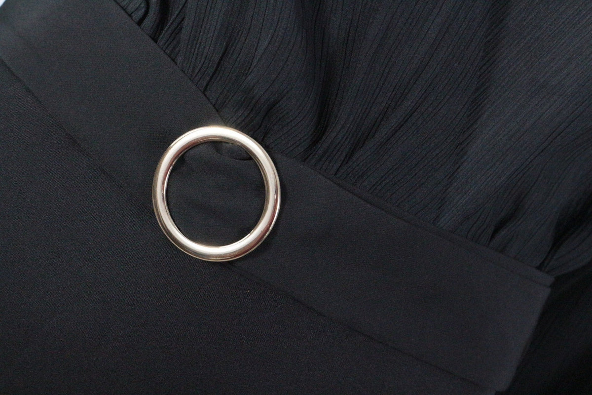 Détail de la robe noire Frippindealz avec tissu plissé et anneau métallique argenté à la taille
