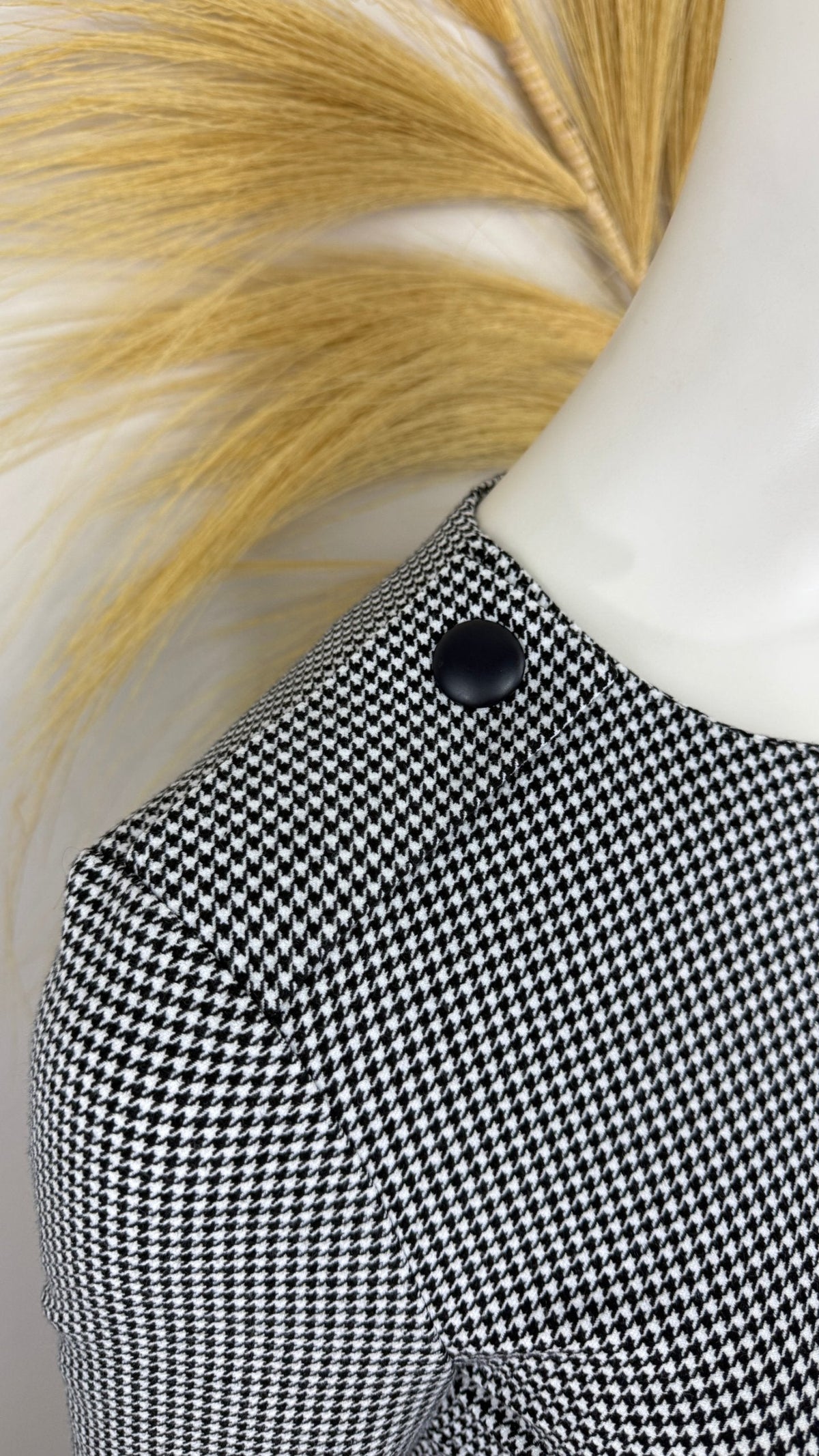 Gros plan sur l'épaule d'une robe Frippindealz à motif pied-de-poule noir et blanc avec un bouton décoratif noir.