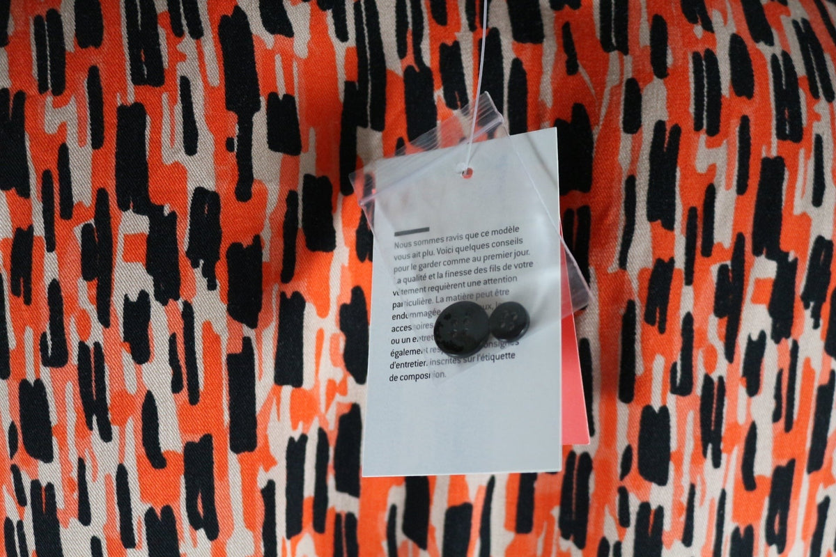 Gros plan sur l'imprimé orange et noir de la robe en viscose Frippindealz avec étiquette et boutons de rechange