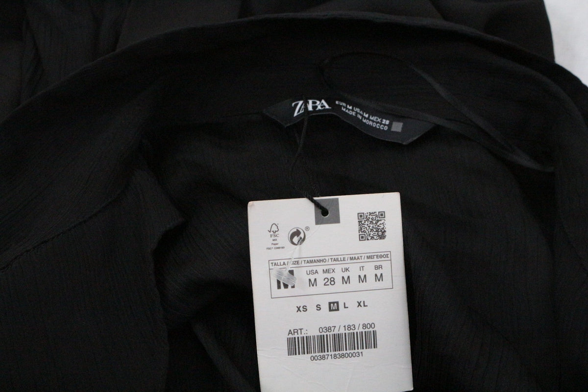 Gros plan sur l'étiquette de marque Zara et l'étiquette de prix d'une robe noire Frippindealz en tissu texturé