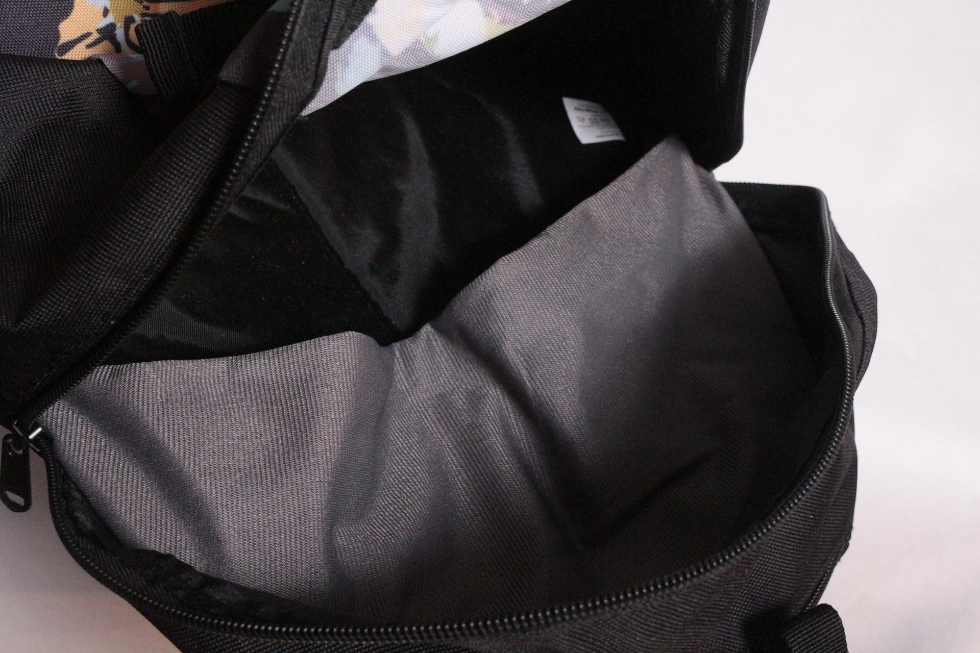 Sac à dos Enuff Skateboards noir en polyester avec doublure intérieure grise et motif floral coloré sur le bord supérieur.