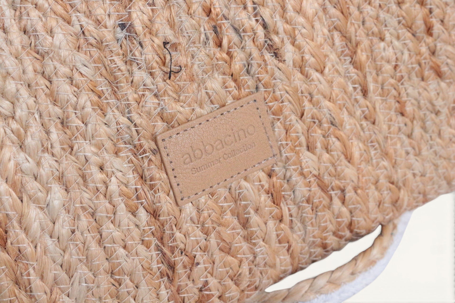 Sac bandoulière Abbacino en jute naturel tressé, avec étiquette en cuir et détails blancs. Parfait pour l'été.