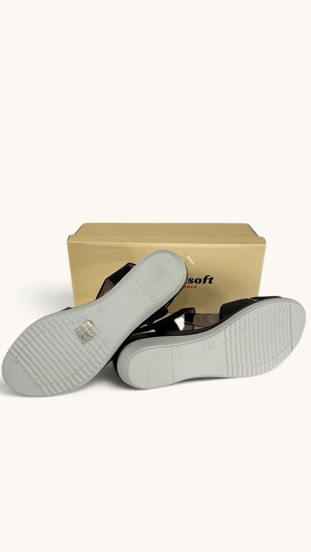 Sandales compensées noires Comfortsoft avec semelles antidérapantes, vues de dessous devant leur boîte Frippindealz