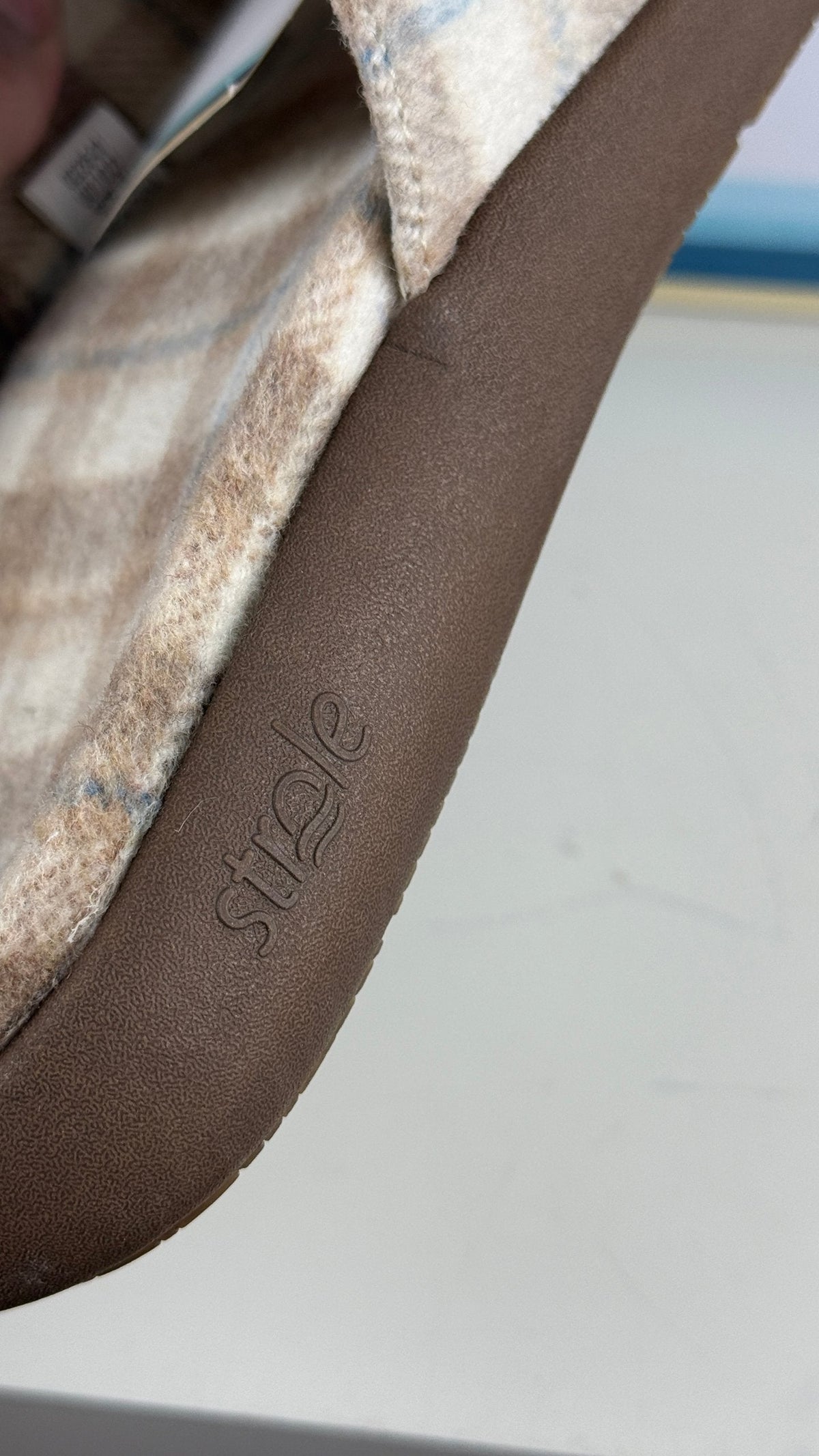 Gros plan sur le logo Strole gravé sur la bordure marron d'une sandale Frippindealz à motif tartan beige et bleu.