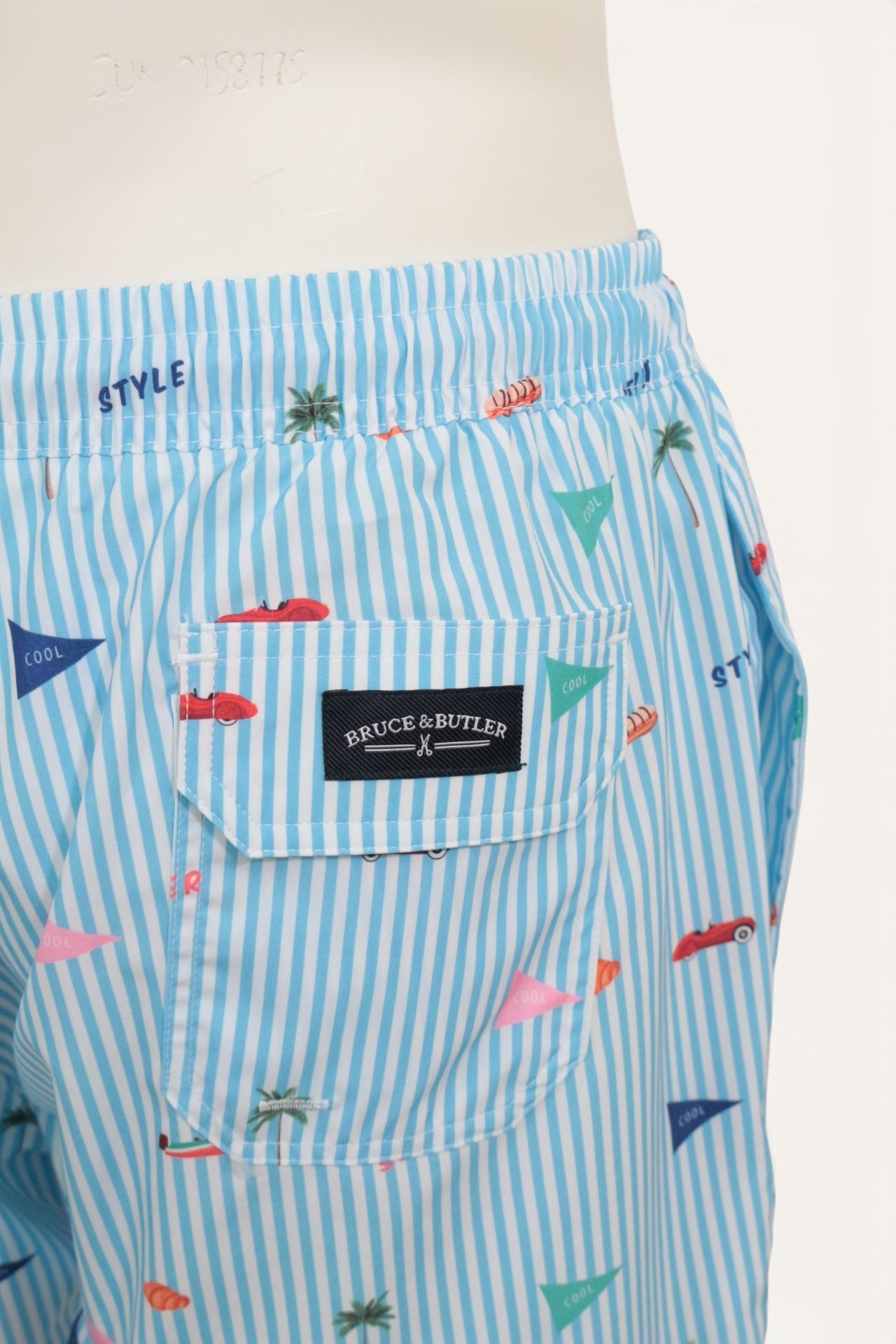 Short de bain Frippindealz Bruce & Butler bleu ciel et blanc à rayures avec motifs estivaux et poche arrière à rabat.