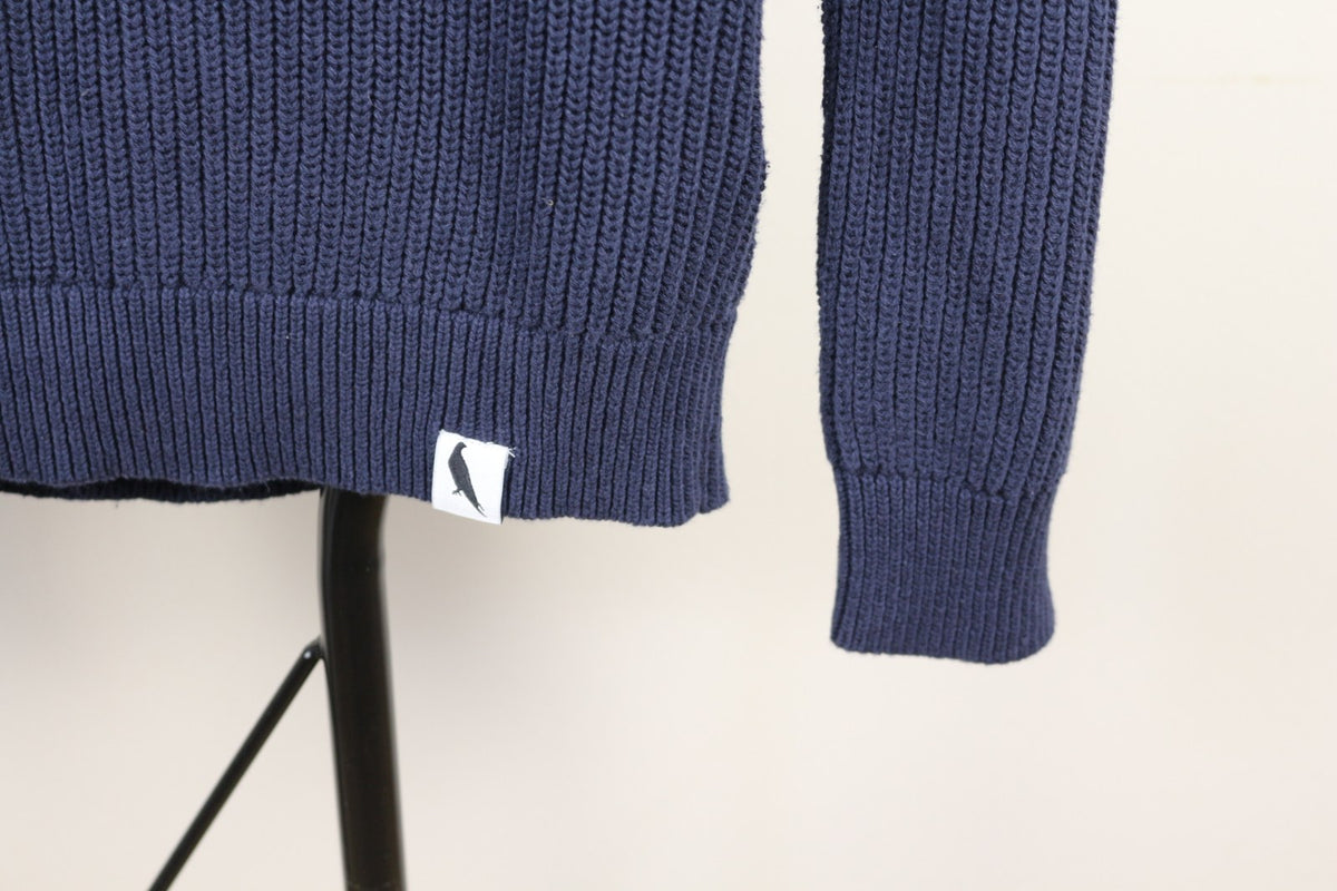 Détail de l'étiquette oiseau tissée et du bas côtelé du pull Peregrine marine – Frippin'Dealz